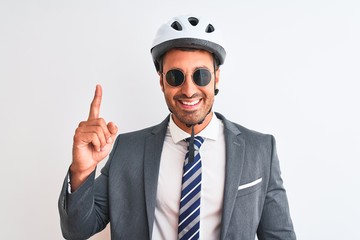 Young handsome business man wearing bike helmet and sunglasses over isolated background surprised with an idea or question pointing finger with happy face, number one