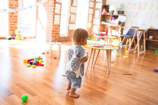 Adorable toddler holding feeding bottle around lots of toys at kindergarten