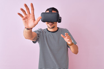 Young man playing video game wearing virtual reality glasses, looking at virtual simulation amazed and smiling happy