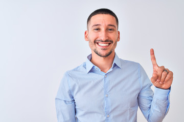 Young handsome business man standing over isolated background showing and pointing up with finger number one while smiling confident and happy.