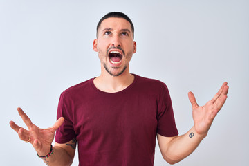 Young handsome man standing over isolated background crazy and mad shouting and yelling with aggressive expression and arms raised. Frustration concept.