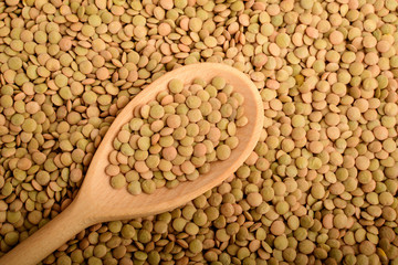 One raw brown wooden spoon with organic fresh green lentil beans on a table in warm light, top view or flat lay of healthy food
