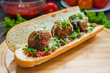sub sandwich with vegan lentil  meatballs tomato sauce grated cheese parsley on cutting board close up