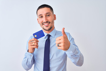 Young business man holding credit card over isolated background happy with big smile doing ok sign, thumb up with fingers, excellent sign