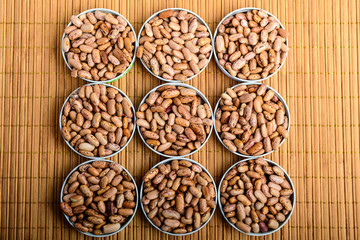 Nine round bowls with organic fresh green red beans on textured bamboo wooden background table in warm light, top view or flat lay of healthy food