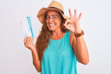 Middle age mature tourist woman holding boarding pass over isolated background doing ok sign with fingers, excellent symbol