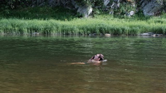 Swimming and swimming in the river and talking on a smartphone. A teenager with a phone lies on the water and floats on his back. Nature, vacation, vacation and modern waterproof devices.