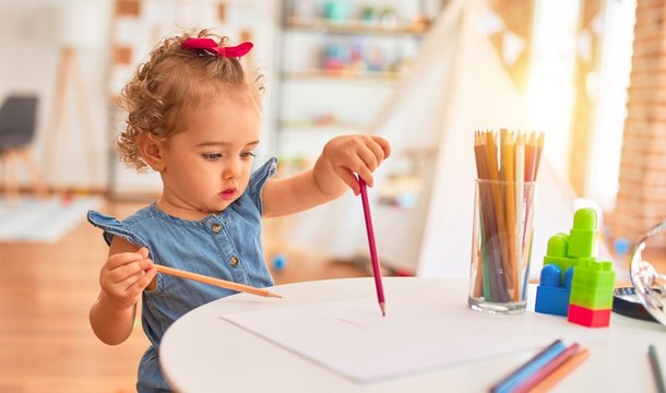 Beautiful caucasian infant playing with toys at colorful playroom. Happy and playful drawing with color pencils at kindergarten.