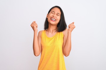 Young chinese woman wearing yellow casual t-shirt standing over isolated white background excited for success with arms raised and eyes closed celebrating victory smiling. Winner concept.