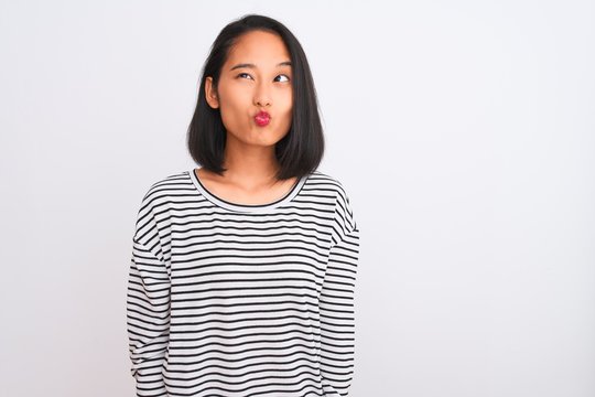 Young chinese woman wearing striped t-shirt standing over isolated white background making fish face with lips, crazy and comical gesture. Funny expression.