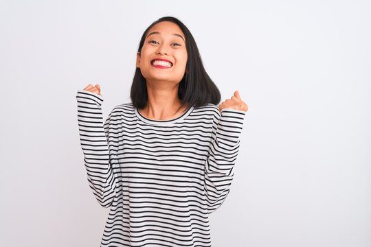 Young chinese woman wearing striped t-shirt standing over isolated white background celebrating surprised and amazed for success with arms raised and open eyes. Winner concept.