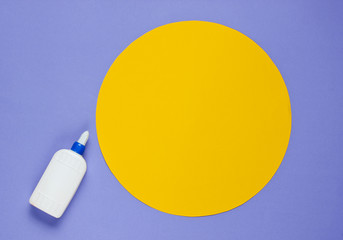 Bottle of glue on a purple paper background with a circle for copy space. Top view