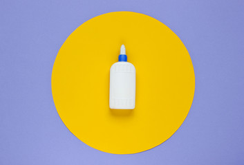 Bottle of glue on a purple paper background with yellow circle. Top view