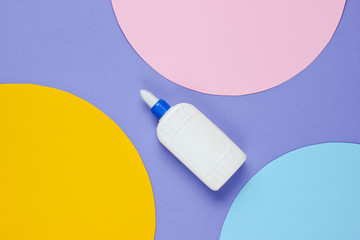 Bottle of glue on a purple paper background with circles. Top view