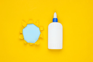 Bottle of glue on yellow paper background with torn hole. Top view