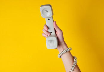 Female hand wrapped in cable holds phone tube against yellow background. Port art. Creative minimalism. Top view