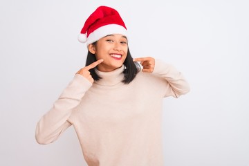 Young beautiful chinese woman wearing Christmas Santa hat over isolated white background smiling cheerful showing and pointing with fingers teeth and mouth. Dental health concept.