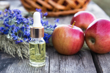 Glass bottle of apple essential oil near fresh apples on a wooden table. Essential oil is used to fill lamps, perfumes and in cosmetics.