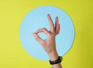 Female hand shows okey gesture on green background with  blue circle. Top view