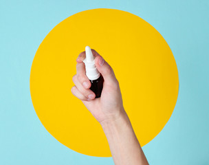 Female hand holds nasal spray on blue background whith yellow circle. Rhinitis treatment