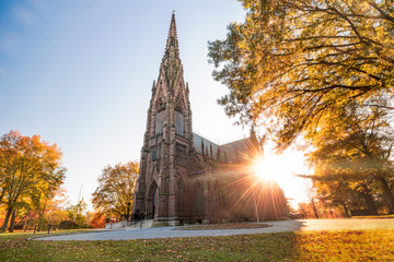 Beautiful Gothic Revival style cathedral at sunset, with golden warm light illuminating the fall foliage around the structure.  - obrazy, fototapety, plakaty
