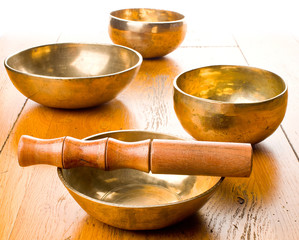 Closeup of four singing bowls and one mallet on a wooden table