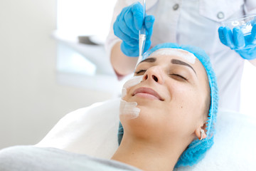 Woman professional doctor beautician applies a mask on a patient's face for skin care. Cosmetic procedures for skin rejuvenation and nutrition