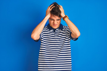 Teenager boy wearing casual t-shirt standing over blue isolated background suffering from headache...