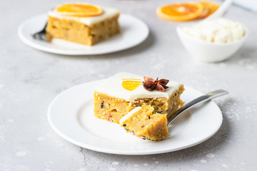 Square pieces of raw spiced carrot cake with orange, nuts and cream cheese frosting. Healthy food.