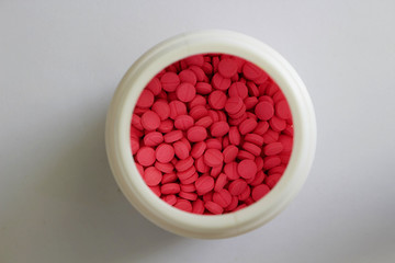 pink round tablets in white jar in medical healthcare drugstore concept,closed up