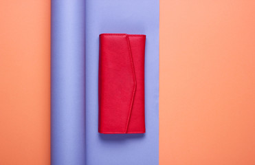Red leather wallet on wrapped paper background. Color trend, minimalistic fashion still life. Top view