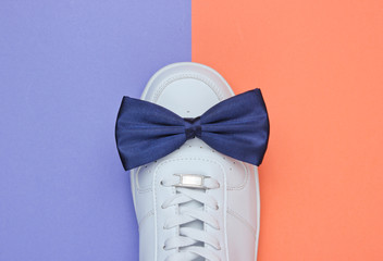 Stylish white sneaker with a bow-tie on a two-color paper background. Minimalistic fashion concept. Top view