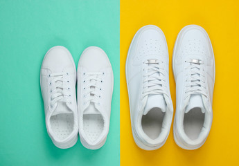 Two pairs of white sneakers on a two-color paper background. Top view