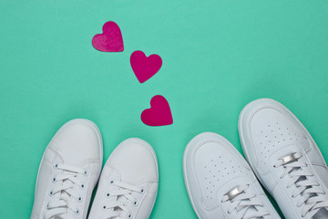 Couple in love. Two pairs of white sneakers and many decorative hearts on blue paper background. Top view