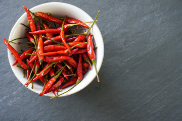 A bowl full of bright red Thai bird chiles on a gray slate background with copy space