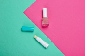 Bottle of nail polish and lipstick on a pink-blue pastel background. Beauty and fashion concept. Top view