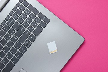 Laptop and SD memory card on pink paper background. Modern gadgets. Top view