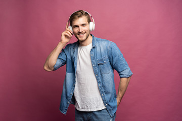 Portrait of happy young man listening to music with headphones isolated over pink background.