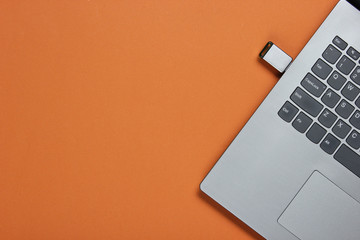 Laptop with flash drive on brown paper background. Studio shot, top view.