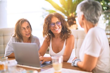 Meeting of middle age women having lunch and drinking coffee. Mature friends smiling happy using laptop at home on a sunny day