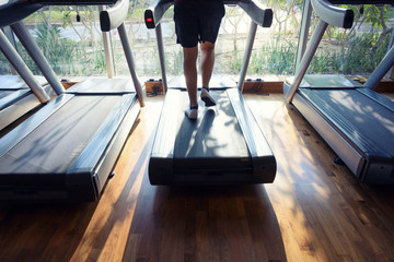 Silhouette motion blurred of sporty man legs running on running machine in the fitness gym room with morning sunlight shine thru window grass and garden background.