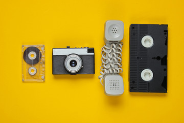 Outdated handset, audio and video cassette, retro camera on a yellow background. Top view