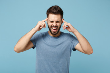 Fototapeta na wymiar Young crazy man in casual clothes posing isolated on blue wall background, studio portrait. People lifestyle concept. Mock up copy space. Screaming, keeping eyes closed, holding index fingers on head.