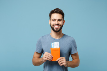 Young smiling attractive man in casual clothes posing isolated on blue wall background, studio portrait. People lifestyle concept. Mock up copy space. Holding in hands passport, boarding pass tickets.