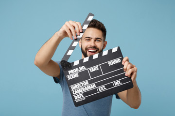 Young cheerful man in casual clothes posing isolated on blue wall background, studio portrait. People lifestyle concept. Mock up copy space. Holding in hands classic black film making clapperboard. - Powered by Adobe