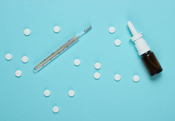 Medical still life on a blue background. Pills, nasal spray, thermometer. Cold treatment. Minimalism