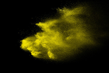 Abstract yellow powder splatter on black background. Freeze motion of yellow powder splash.