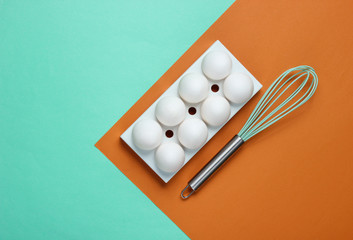Tray with white chicken eggs and whisk on colored background. Minimalistic food concept. Top view