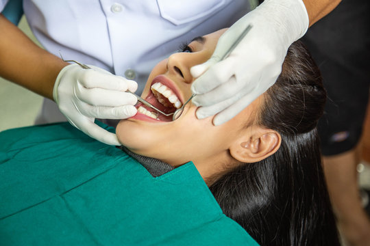 Dentist examining teeth of beautiful young smiling Asian woman in hospital clinic dental health care concept