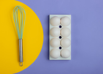 Tray with white chicken eggs and whisk on blue background. Minimalistic food concept.
